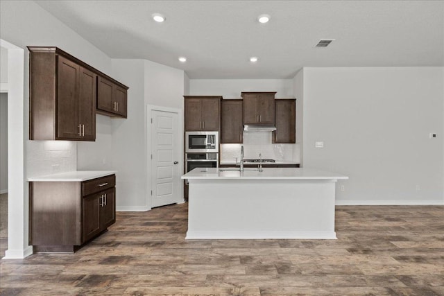 240 Camino Verde Dr, San Marcos, TX 78666 - kitchen with appliances with stainless steel finishes, under cabinet range hood, decorative backsplash, a center island with sink, and dark brown cabinets