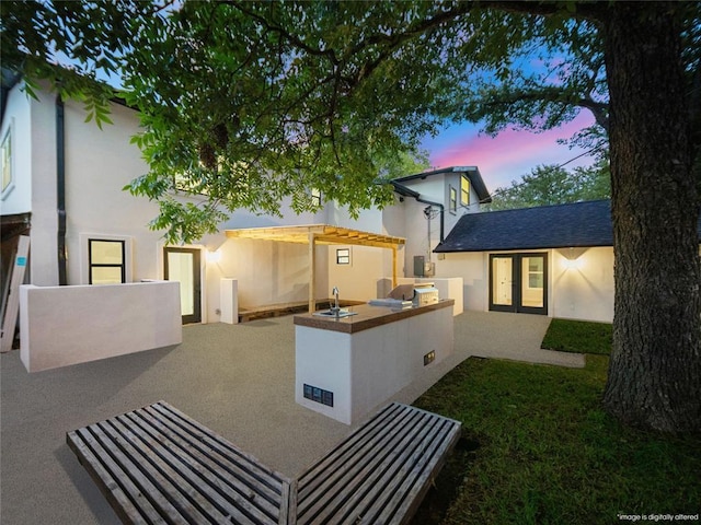 2004 N Cuernavaca Dr, Austin, TX 78733 - back of property at dusk featuring area for grilling, stucco siding, a patio area, and french doors