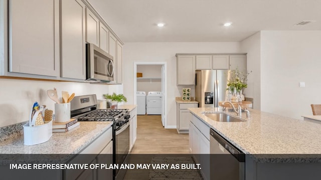 272 Morning Glory Loop, Kyle, TX 78640 - kitchen with appliances with stainless steel finishes, a sink, washer and dryer, light wood finished floors, and a center island with sink