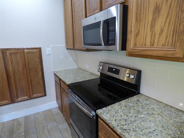 918 Crystal Brook Cv, New Braunfels, TX 78130 - kitchen with stainless steel appliances, brown cabinetry, tasteful backsplash, and light stone countertops