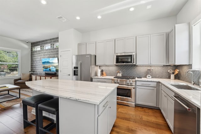 kitchen with high end appliances, a sink, a center island, light stone countertops, and backsplash