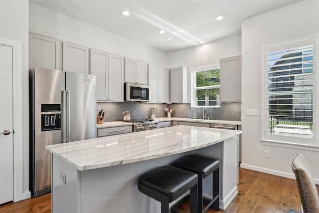 kitchen with appliances with stainless steel finishes, backsplash, a kitchen bar, a center island, and light stone countertops