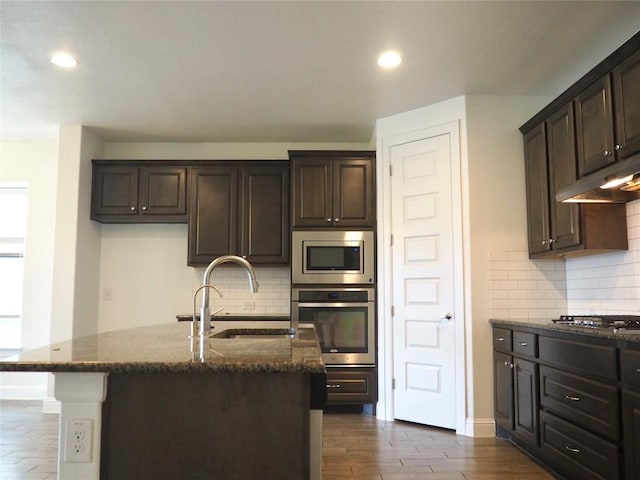 1902 Aves Cv, Pflugerville, TX 78660 - kitchen featuring stainless steel appliances, a sink, dark stone counters, dark brown cabinets, and recessed lighting