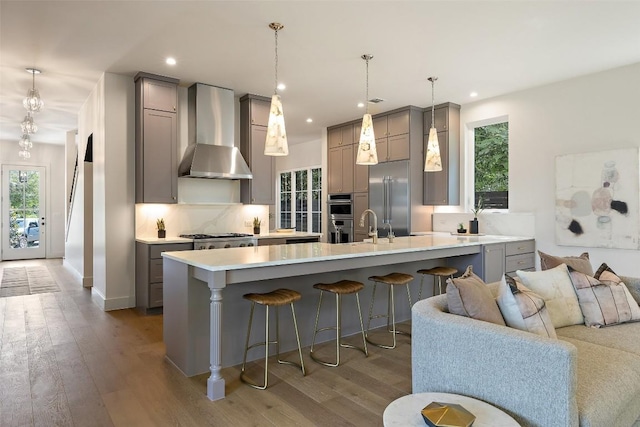 4600 Parkdale Pl, Austin, TX 78745 - kitchen with gray cabinetry, wall chimney exhaust hood, appliances with stainless steel finishes, a kitchen bar, and recessed lighting