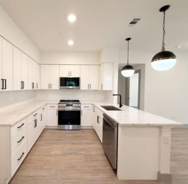 2450 Wickersham Ln Unit 1926, Austin, TX 78741 - kitchen with stainless steel appliances, a sink, a peninsula, light wood-style flooring, and light stone countertops