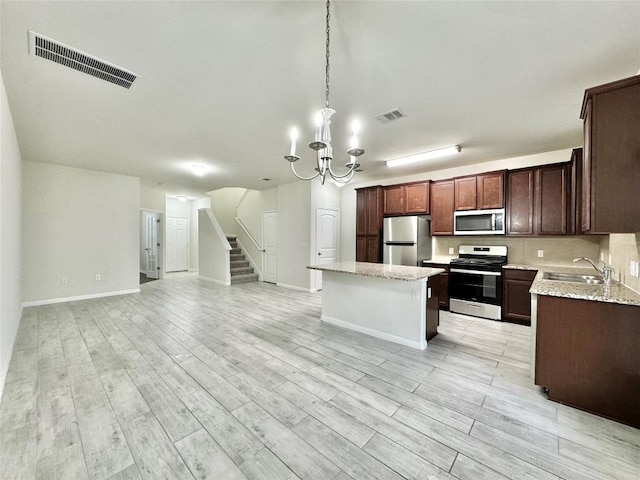 513 N Heatherwilde Blvd, Pflugerville, TX 78660 - kitchen with appliances with stainless steel finishes, a sink, open floor plan, a kitchen island, and light wood-style flooring