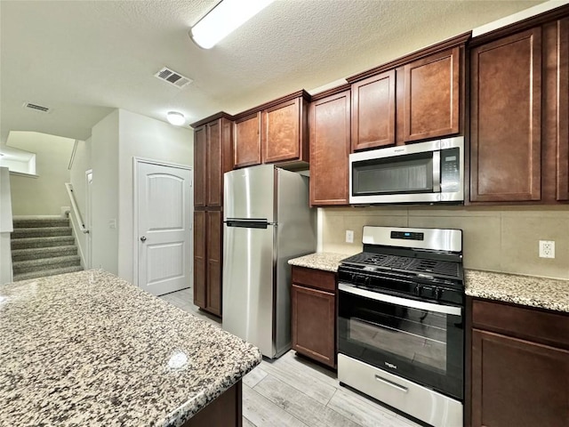 513 N Heatherwilde Blvd, Pflugerville, TX 78660 - kitchen with appliances with stainless steel finishes, light stone counters, light wood finished floors, and decorative backsplash
