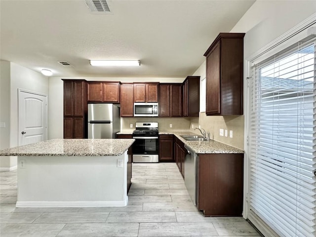 513 N Heatherwilde Blvd, Pflugerville, TX 78660 - kitchen featuring appliances with stainless steel finishes, a sink, a center island, light stone counters, and dark brown cabinetry
