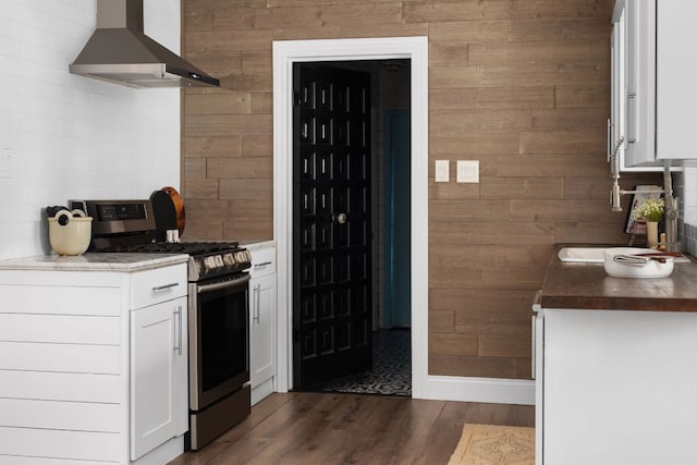 2403 Little John Ln, Austin, TX 78704 - kitchen featuring stainless steel range with gas stovetop, wall chimney exhaust hood, wood walls, white cabinetry, and dark wood-type flooring