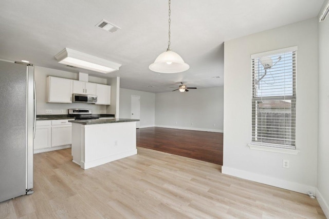 100 Blanco Woods Blvd, Elgin, TX 78621 - kitchen with stainless steel appliances, dark countertops, light wood-type flooring, white cabinetry, and baseboards