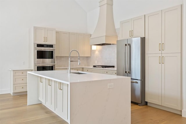 402 Fife Dr, Spicewood, TX 78669 - kitchen with appliances with stainless steel finishes, custom range hood, a sink, tasteful backsplash, and light wood-type flooring