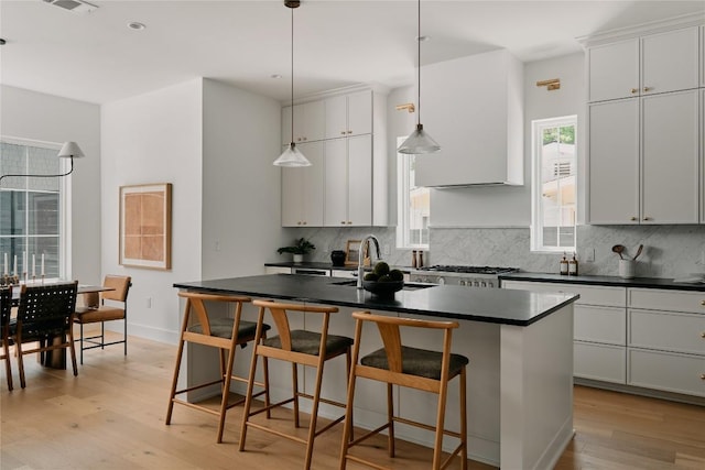 113 Nelray Blvd Unit 1, Austin, TX 78751 - kitchen with a sink, dark countertops, light wood-type flooring, decorative backsplash, and a center island with sink