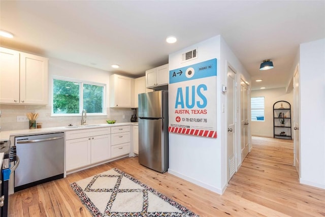 3801 Wilson St, Austin, TX 78704 - kitchen with stainless steel appliances, a sink, light wood-style floors, white cabinets, and backsplash