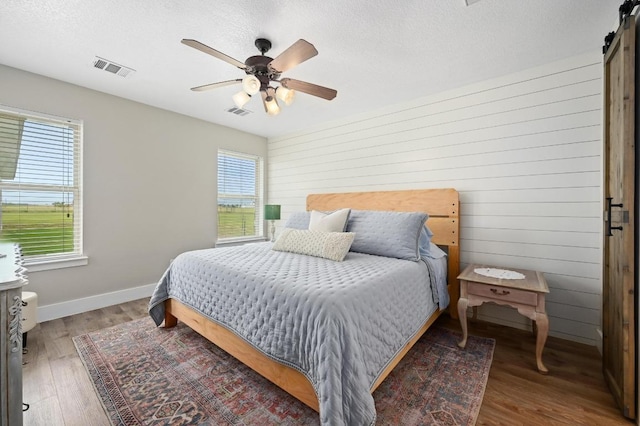 1011 County Road 149, Georgetown, TX 78626 - bedroom with multiple windows, wood finished floors, ceiling fan, a textured ceiling, and a barn door