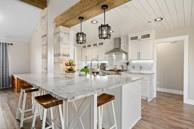 1011 County Road 149, Georgetown, TX 78626 - kitchen with wall chimney range hood, decorative backsplash, light wood-style flooring, light stone counters, and a breakfast bar area