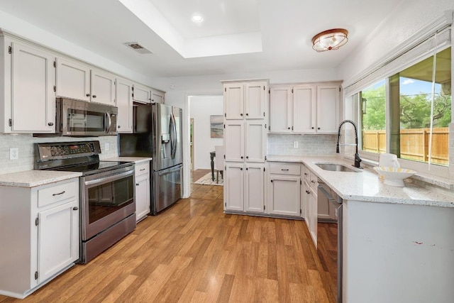 9417 Longvale Dr, Austin, TX 78729 - kitchen with appliances with stainless steel finishes, a sink, light wood-style floors, a raised ceiling, and backsplash