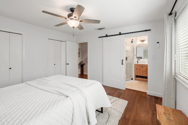 9417 Longvale Dr, Austin, TX 78729 - bedroom featuring a barn door, dark wood-type flooring, a sink, multiple closets, and ceiling fan