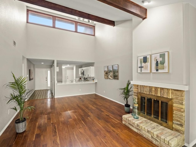 3700 Steck Ave, Austin, TX 78759 - unfurnished living room with a high ceiling, dark wood finished floors, baseboards, a brick fireplace, and beam ceiling