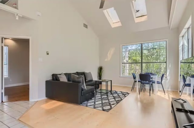 1202 Loma Dr, Austin, TX 78741 - living room with high vaulted ceiling, a skylight, light wood-style flooring, and baseboards