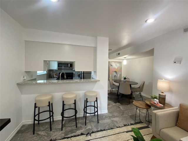 3819 Southway Dr, Austin, TX 78704 - kitchen featuring stainless steel microwave, a breakfast bar area, white cabinets, a sink, and baseboards