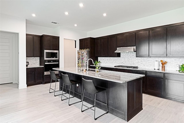216 Reata Ridge Loop, Liberty Hill, TX 78642 - kitchen with appliances with stainless steel finishes, under cabinet range hood, a sink, a kitchen breakfast bar, and decorative backsplash