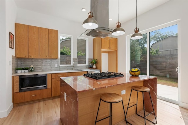 106 W Croslin St Unit B, Austin, TX 78752 - kitchen featuring stainless steel microwave, black gas stovetop, island range hood, light wood-style floors, and backsplash