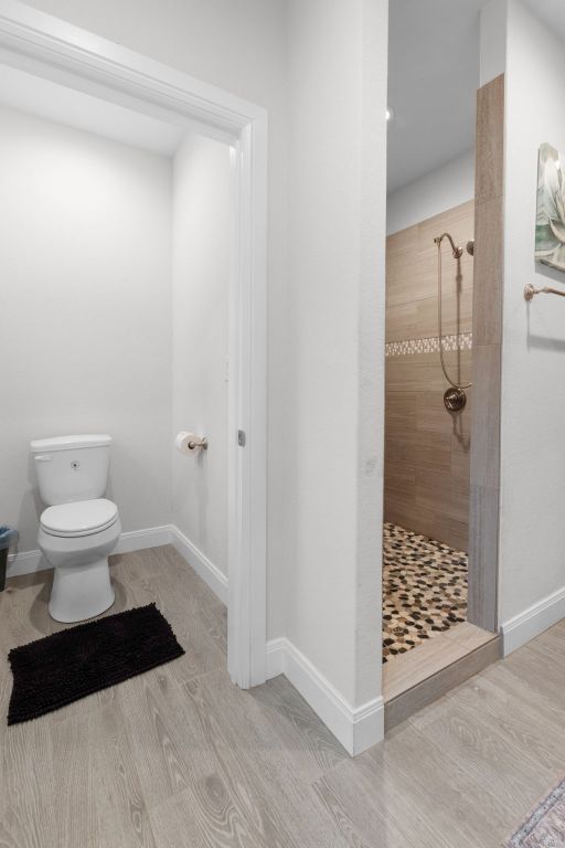 110 Lakecliff Cv, Kingsland, TX 78639 - bathroom featuring a tile shower, toilet, wood finished floors, and baseboards