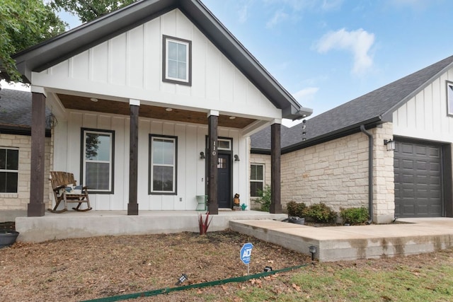 110 Lakecliff Cv, Kingsland, TX 78639 - view of front of property featuring board and batten siding, covered porch, an attached garage, a shingled roof, and stone siding
