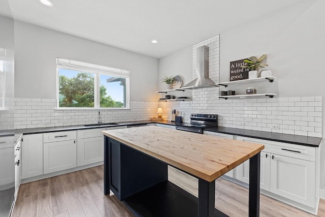 20702 Post Oak Dr, Lago Vista, TX 78645 - kitchen with black electric range oven, wall chimney exhaust hood, open shelves, a sink, and light wood-style floors