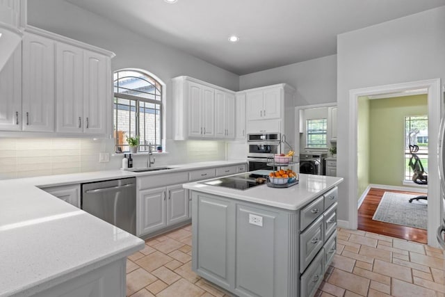 205 Champion Dr, Lakeway, TX 78734 - kitchen with appliances with stainless steel finishes, washing machine and clothes dryer, white cabinetry, a center island, and stone tile floors