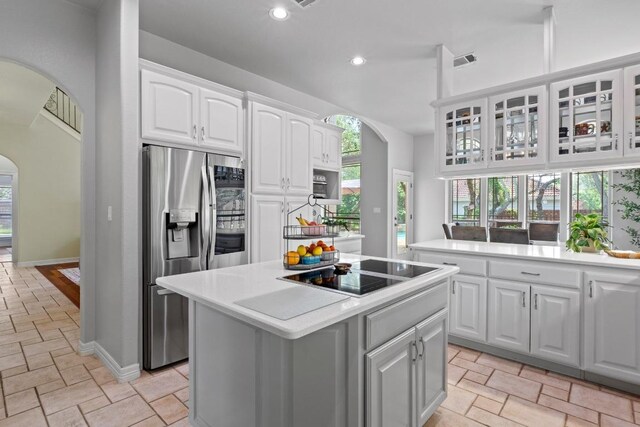 205 Champion Dr, Lakeway, TX 78734 - kitchen featuring arched walkways, stainless steel fridge with ice dispenser, black electric cooktop, a kitchen island, and stone tile flooring