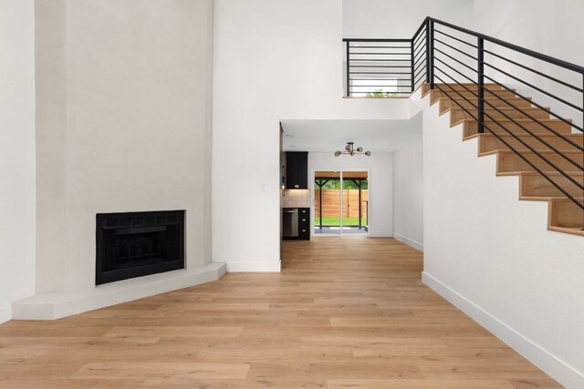 2716 Gettysburg Dr, Austin, TX 78745 - unfurnished living room with a towering ceiling, stairway, baseboards, a fireplace with raised hearth, and wood finished floors