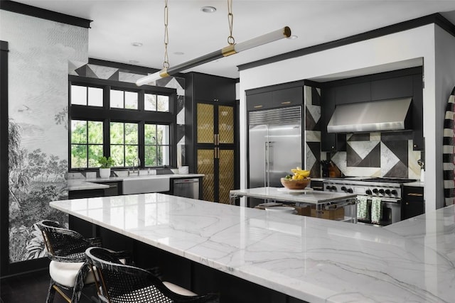 102 Crestwood Ct, Austin, TX 78746 - kitchen with exhaust hood, high quality appliances, light stone counters, backsplash, and dark cabinetry