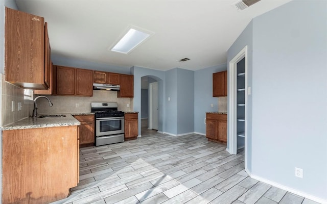 3907 Sojourner St, Austin, TX 78725 - kitchen with stainless steel gas range oven, a sink, under cabinet range hood, arched walkways, and backsplash