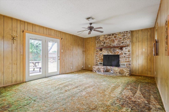 4412 Briar Cliff Rd, Temple, TX 76502 - unfurnished living room featuring a ceiling fan, a stone fireplace, wood walls, carpet flooring, and a textured ceiling