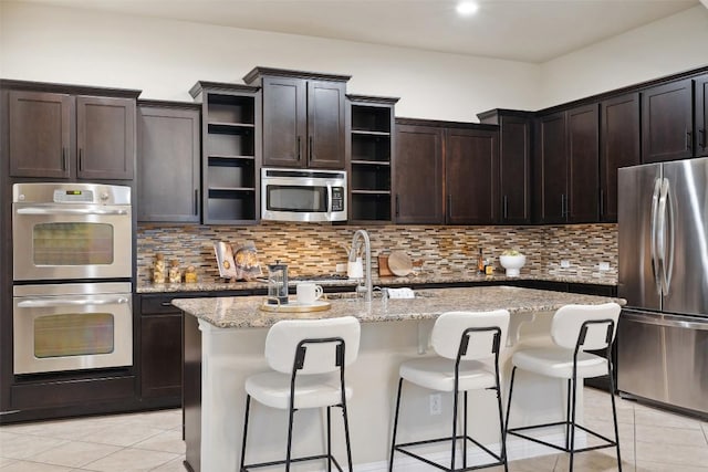 2944 Castellan Ln, Round Rock, TX 78665 - kitchen featuring appliances with stainless steel finishes, open shelves, light tile patterned flooring, decorative backsplash, and a kitchen island with sink