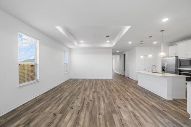 13505 Cerro Castellan Trce, Manor, TX 78653 - unfurnished living room with wood finished floors, recessed lighting, a sink, a raised ceiling, and baseboards
