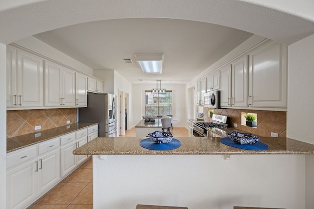 3619 Fossilwood Way, Round Rock, TX 78681 - kitchen with appliances with stainless steel finishes, a peninsula, arched walkways, white cabinets, and decorative backsplash