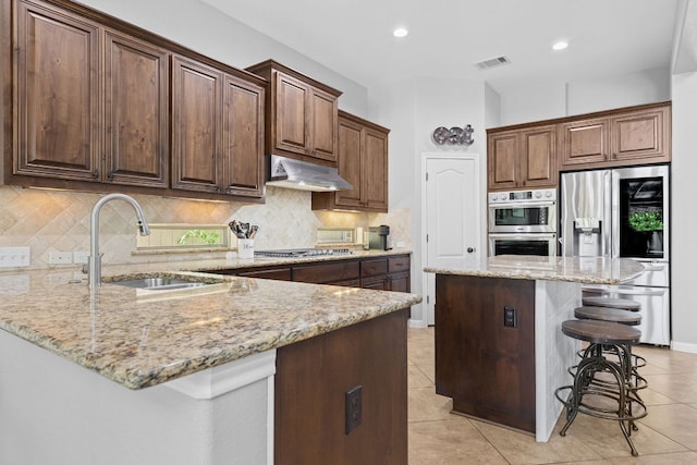 2516 Rusty Spur, Leander, TX 78641 - kitchen featuring stainless steel appliances, under cabinet range hood, a kitchen bar, a sink, and light stone counters