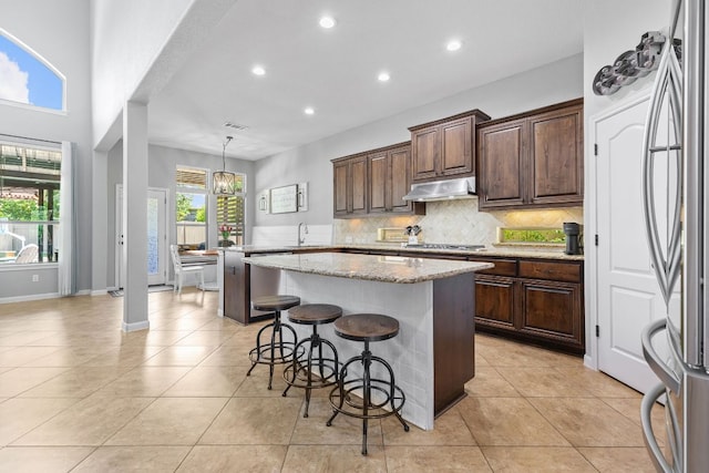 2516 Rusty Spur, Leander, TX 78641 - kitchen with a sink, a center island, under cabinet range hood, a breakfast bar area, and decorative backsplash