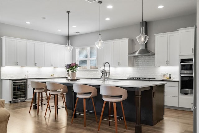 8112 Silhouette St, Austin, TX 78744 - kitchen featuring beverage cooler, a sink, wall chimney exhaust hood, a kitchen island with sink, and double oven
