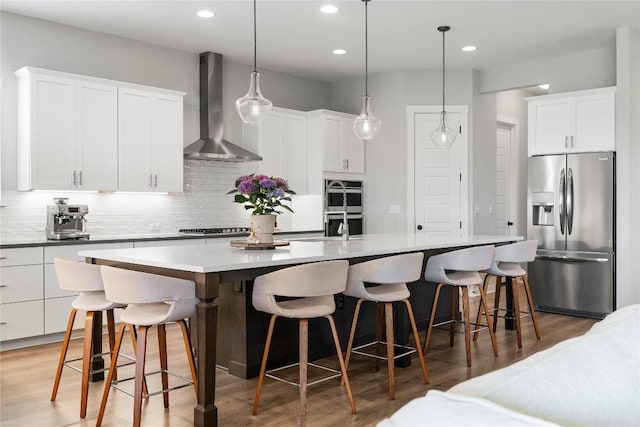 8112 Silhouette St, Austin, TX 78744 - kitchen featuring stainless steel appliances, wall chimney exhaust hood, decorative backsplash, a kitchen island with sink, and light wood finished floors