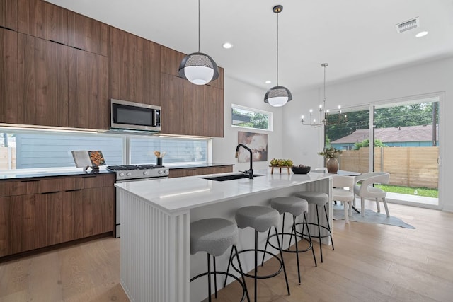 2114 Haskell St, Austin, TX 78702 - kitchen with stainless steel appliances, modern cabinets, light wood-style flooring, a kitchen breakfast bar, and a kitchen island with sink