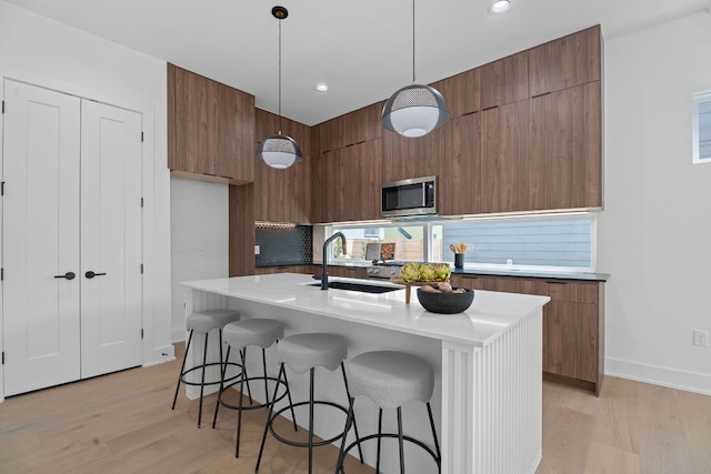 2114 Haskell St, Austin, TX 78702 - kitchen featuring modern cabinets, stainless steel microwave, light wood finished floors, light countertops, and brown cabinetry