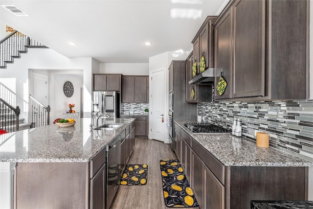 306 Pulitzer Dr, Hutto, TX 78634 - kitchen with appliances with stainless steel finishes, wood finished floors, under cabinet range hood, dark brown cabinets, and a center island with sink