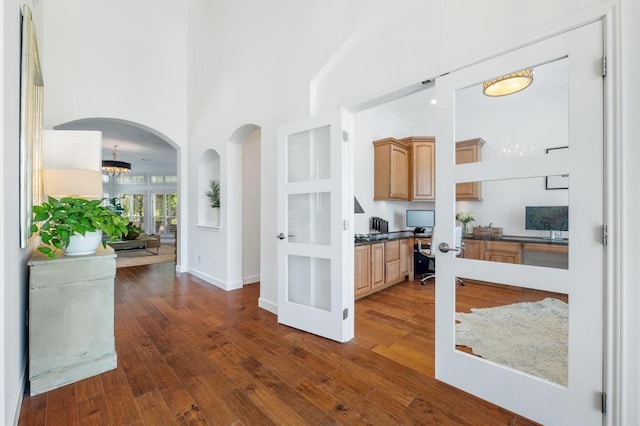 1701 Mira Vis, Leander, TX 78641 - kitchen featuring dark wood-style flooring, built in study area, a towering ceiling, dark countertops, and arched walkways