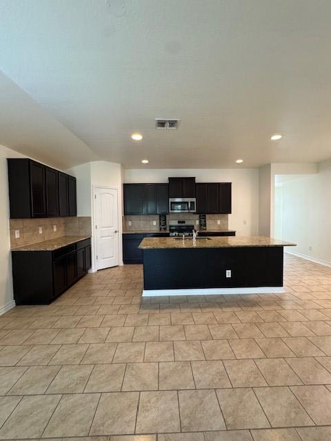 5511 Toledo Farm, San Antonio, TX 78222 - kitchen with stainless steel microwave, backsplash, dark cabinets, a center island with sink, and recessed lighting