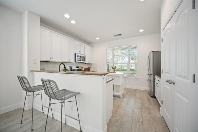 206 Skinner, Kyle, TX 78640 - kitchen with appliances with stainless steel finishes, white cabinets, light wood-style floors, decorative backsplash, and recessed lighting