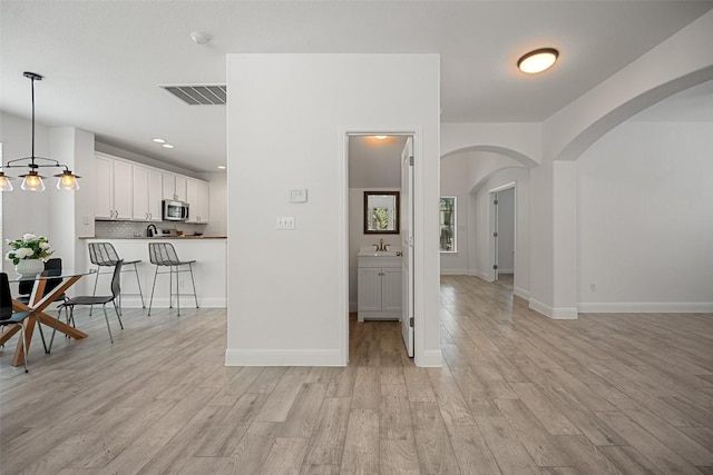 206 Skinner, Kyle, TX 78640 - kitchen featuring stainless steel microwave, arched walkways, white cabinets, and light wood-type flooring