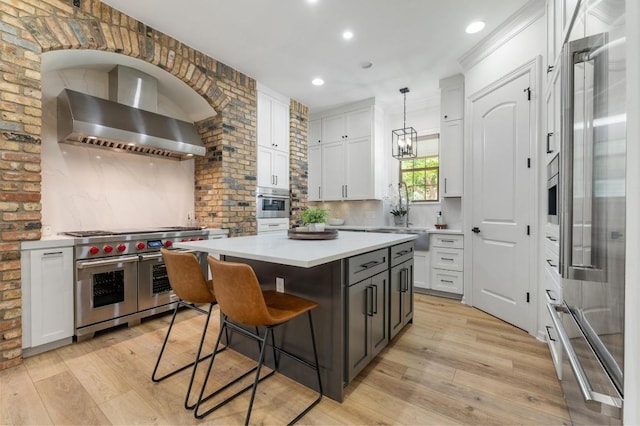 7 Sunview Rd, The Hills, TX 78738 - kitchen with premium appliances, wall chimney exhaust hood, light wood-style flooring, a kitchen island, and white cabinetry